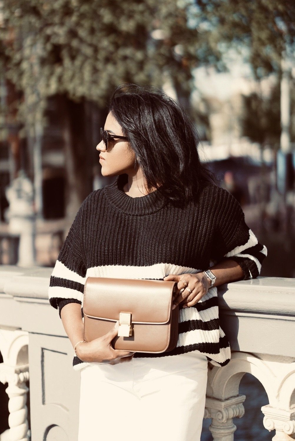 Close up of Sachini wearing black and white knitwear, white culottes holding a brown Celine bag