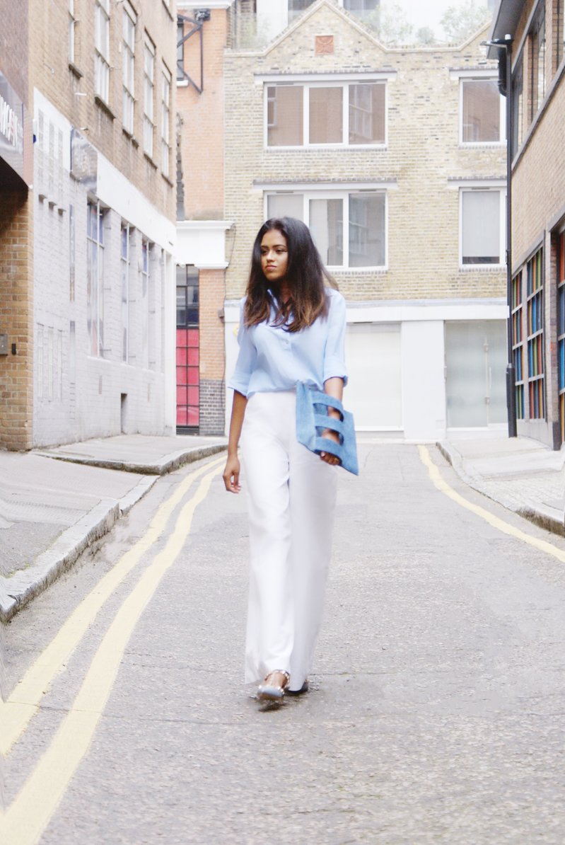 Sachini wearing a blue top, Valentino shoes and white trousers holding a jean colour Embellished Truth bag