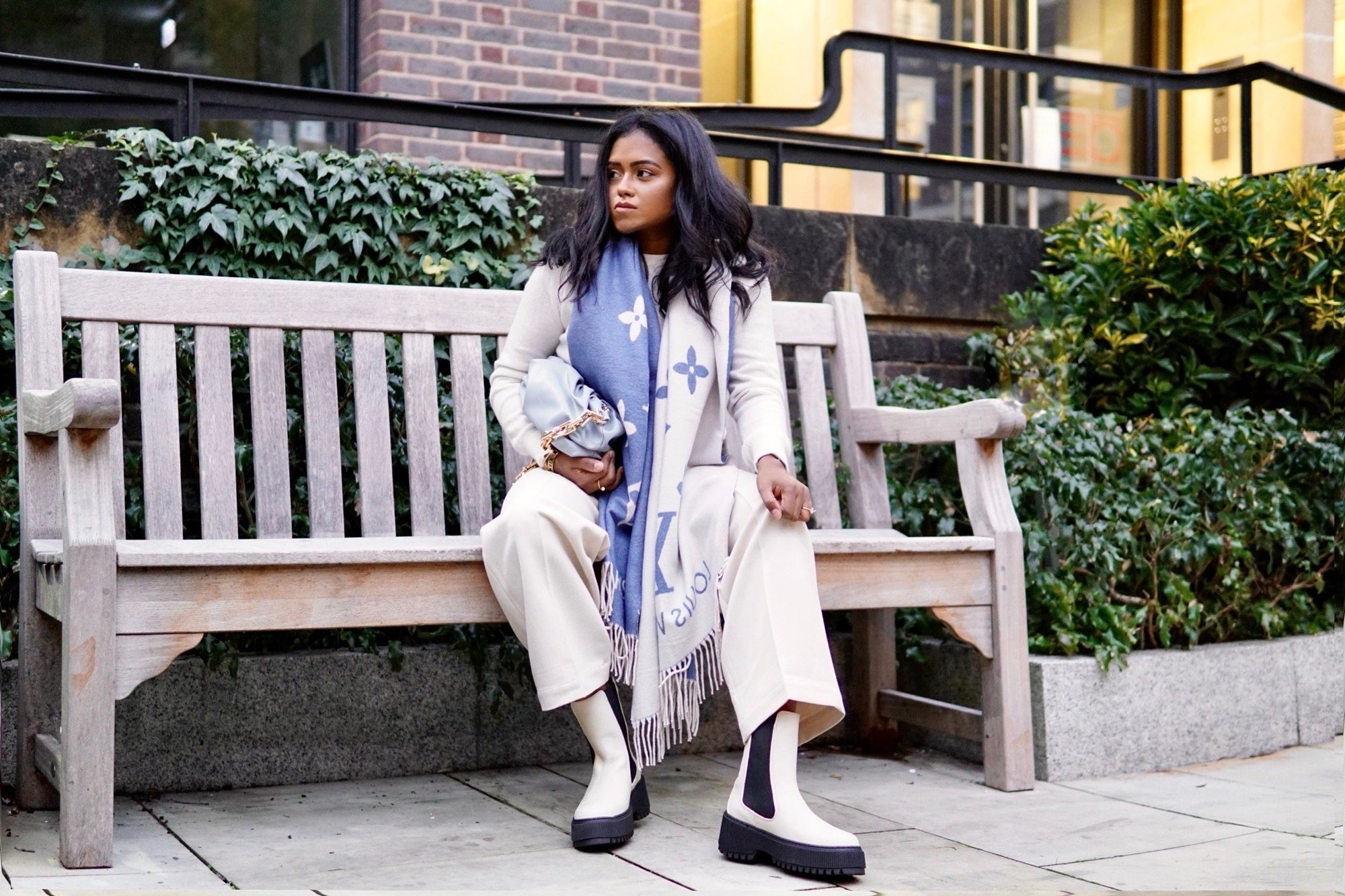 Sachini sitting on a bench with a Louis Vuitton scarf and & Other Stories boots