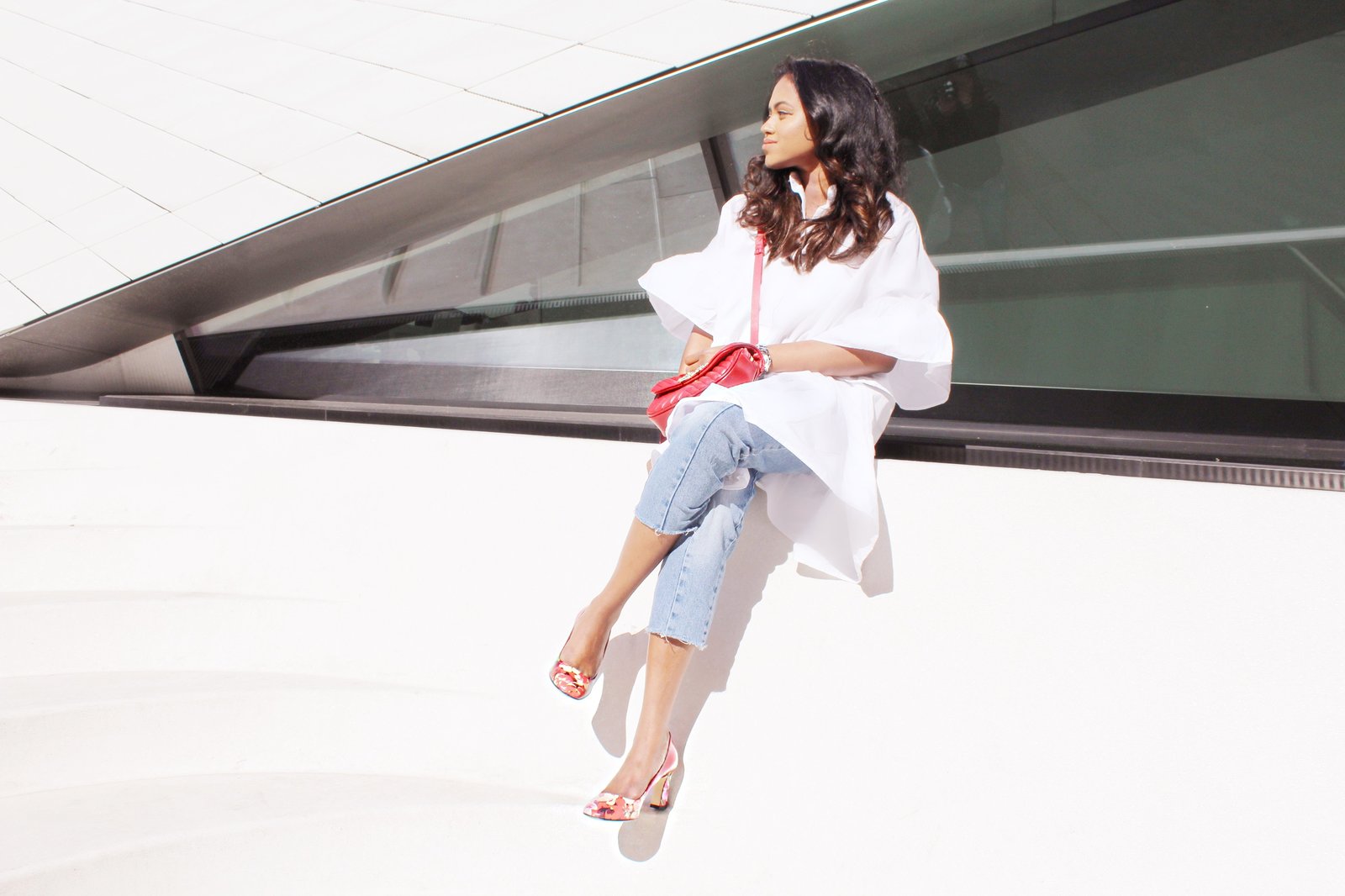 Sachini sitting wearing a white dress, red Gucci shoes and Levi's jeans