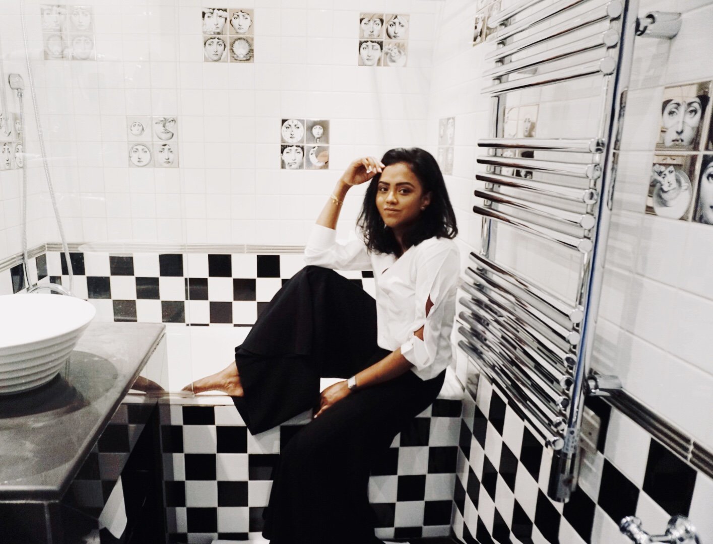 Sachini sitting on a black and white bath wearing a white shirt and black trousers