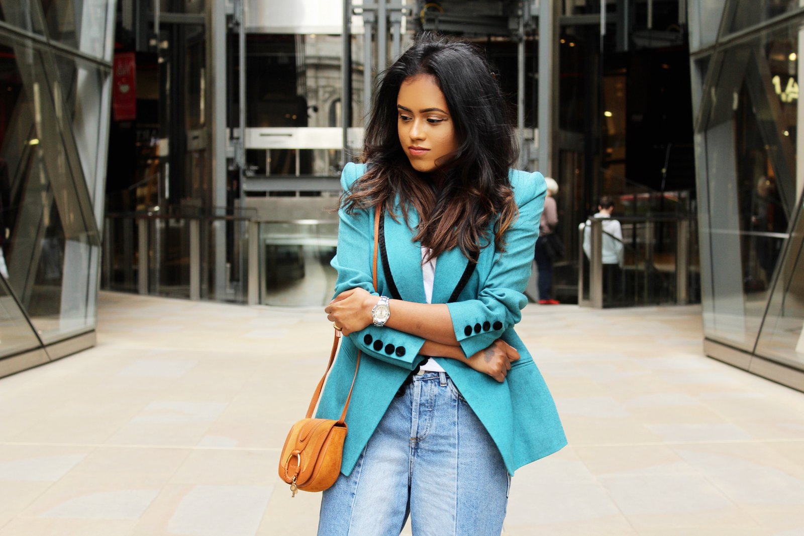 Close up of Sachini standing in a shopping street wearing a light blue Fendi vintage blazer, blue jeans with a brown handbag