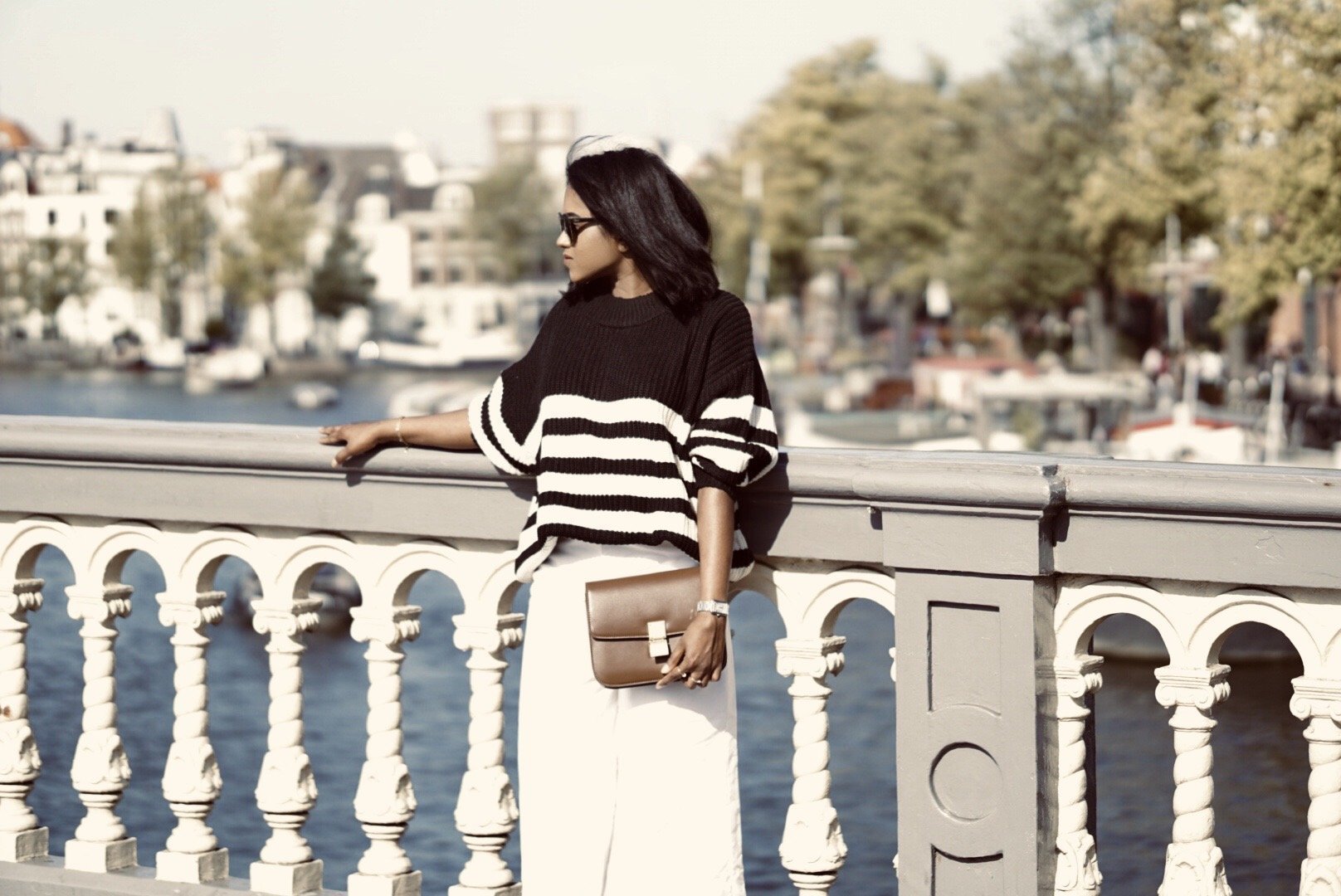 Sachini in Amsterdam on a bridge wearing black and white knitwear, white culottes holding a brown Celine bag
