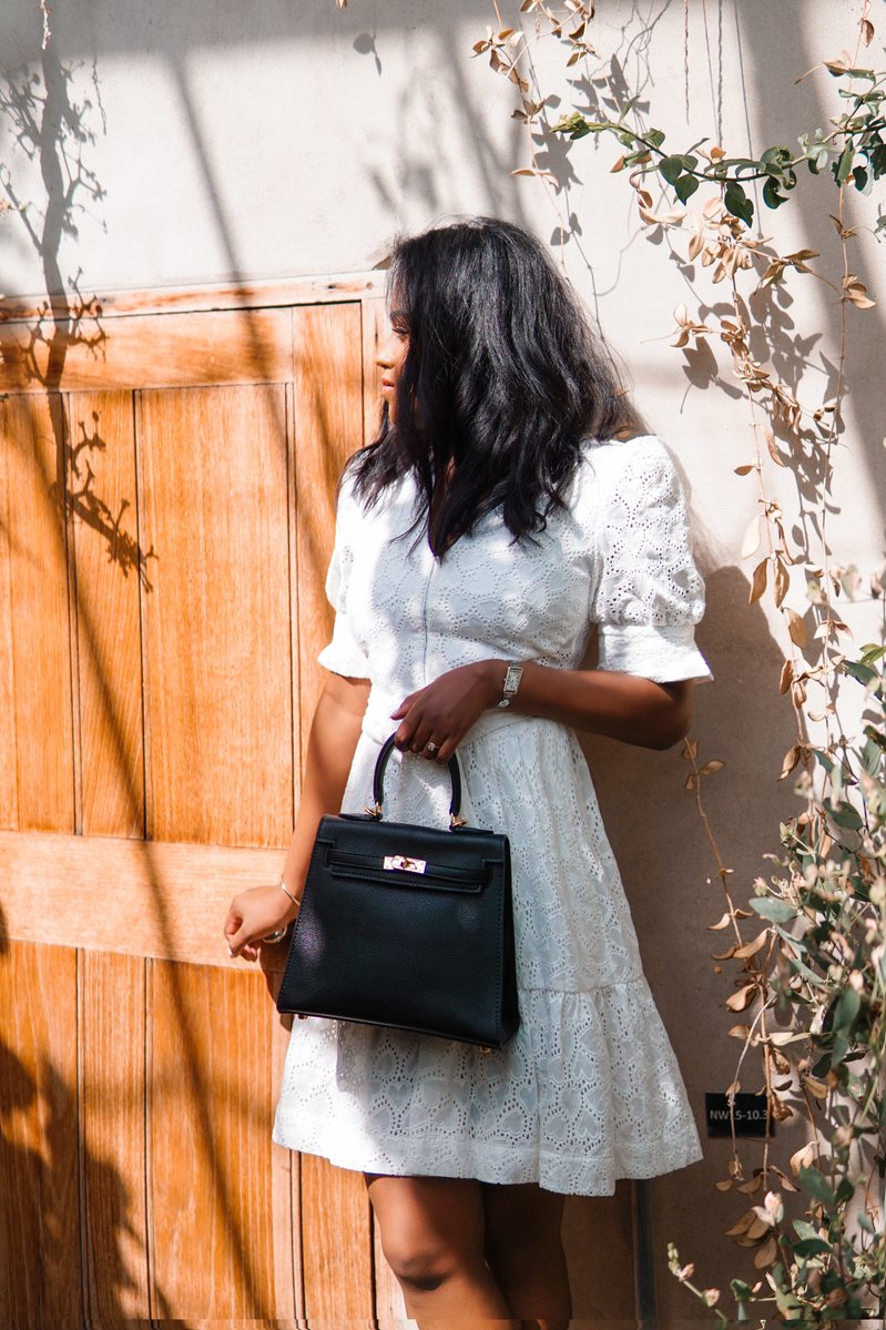 Sachini wearing a white dress holding a black Hermès Kelly bag