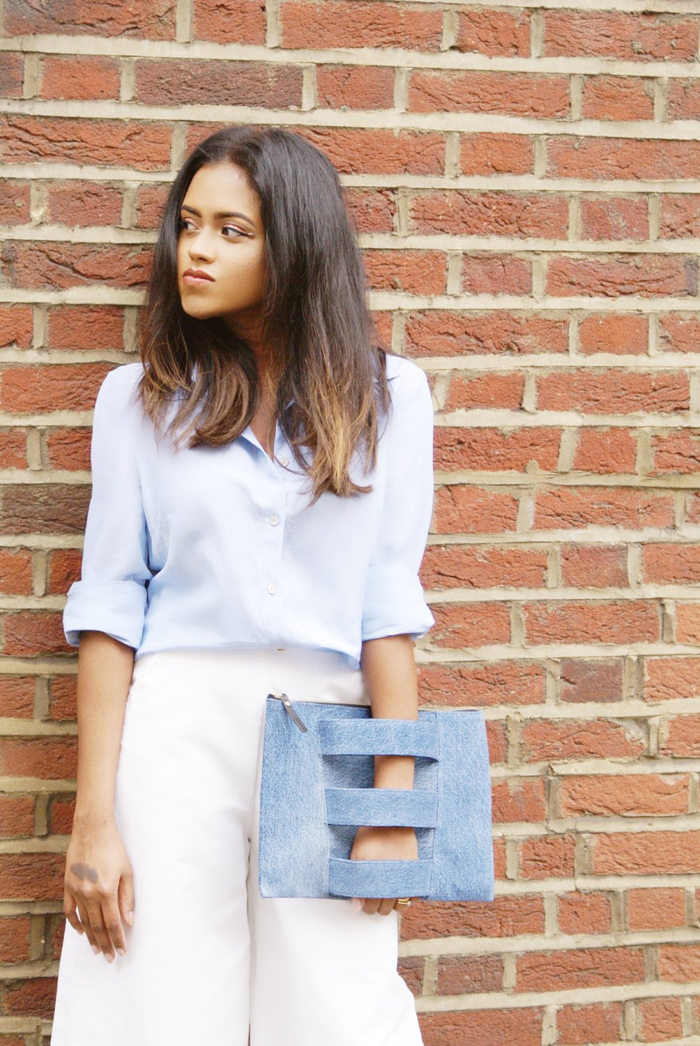 Sachini wearing a blue top and white trousers holding a jean colour Embellished Truth bag
