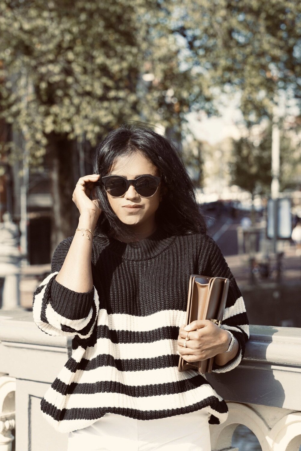 Close up of Sachini wearing black and white knitwear, white culottes holding a brown Celine bag