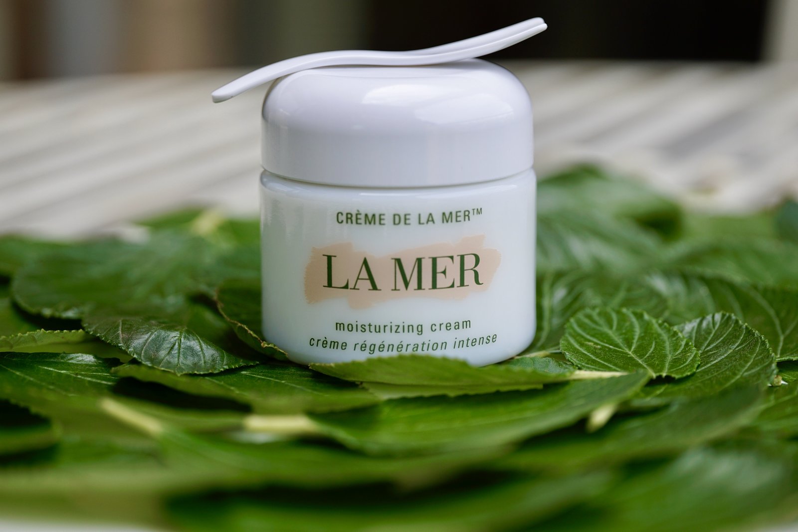 Close up of an open crème de la mer cream pot on a bed of leaves