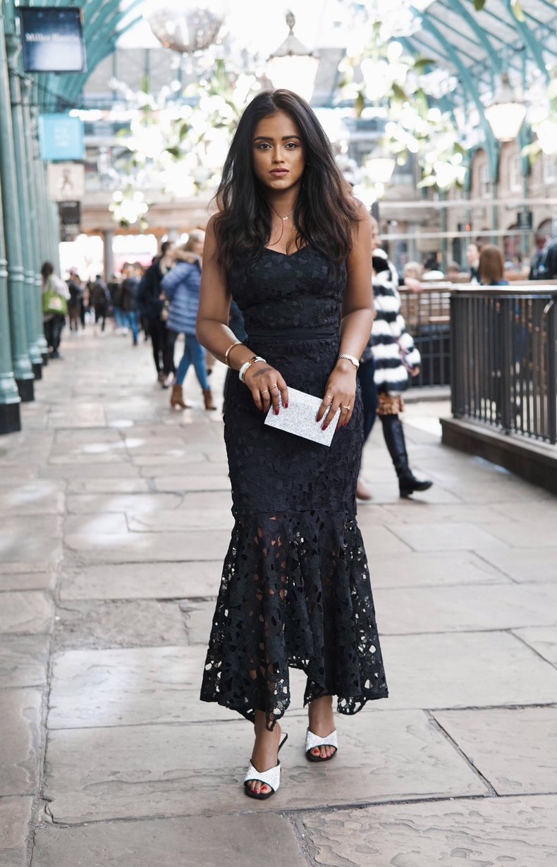 Sachini wearing a black Chi Chi London dress with people walking in the background