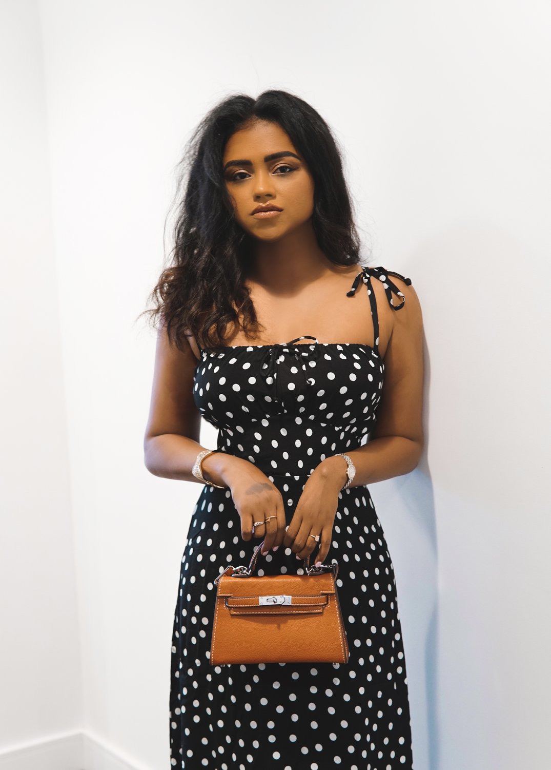 Sachini wearing a black and white Reformation polkadot dress holding a brown Hermès mini Kelly bag