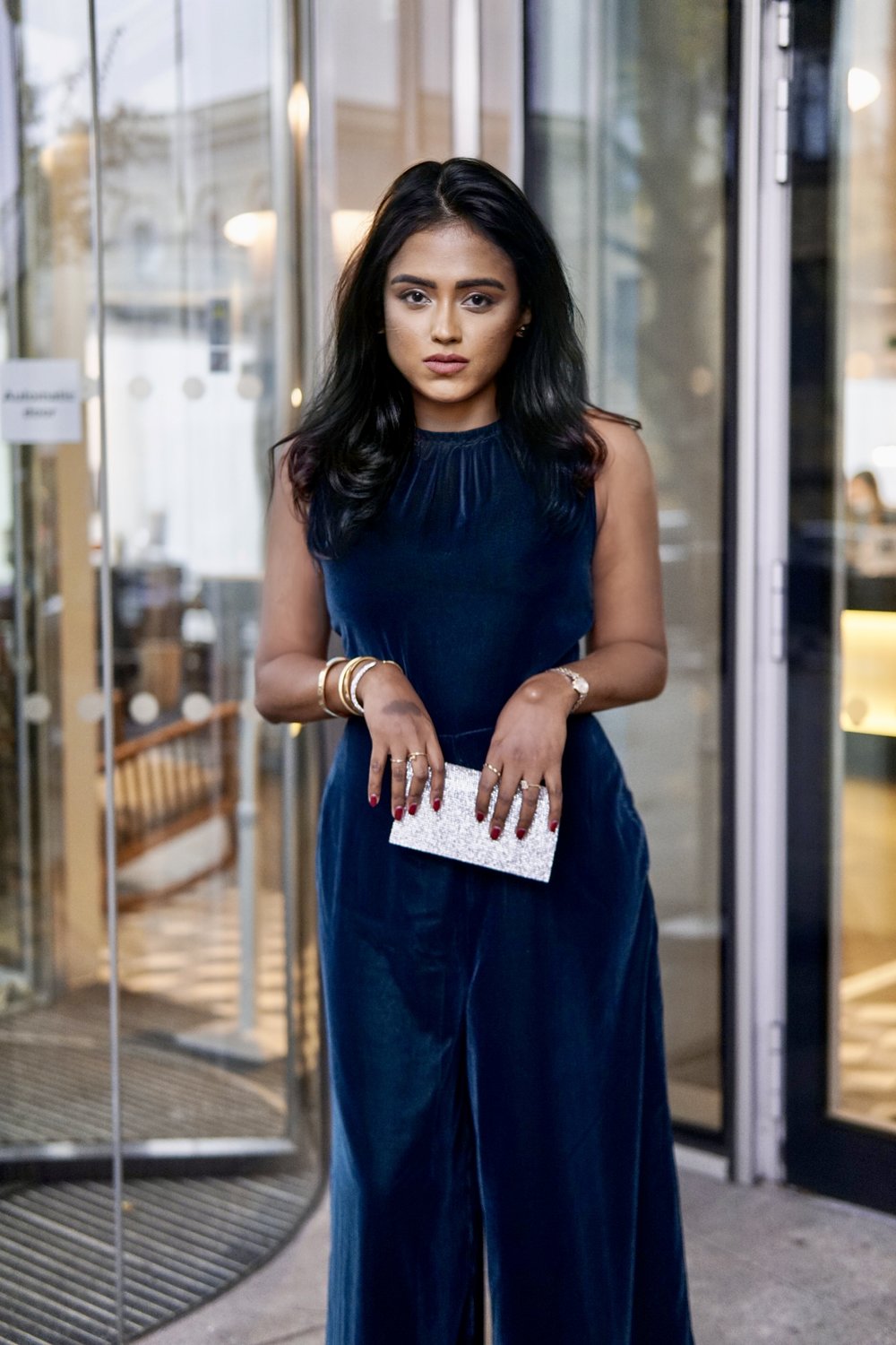 Sachini standing in front of a glass window wearing a navy colour Albaray dress holding a small silver handbag