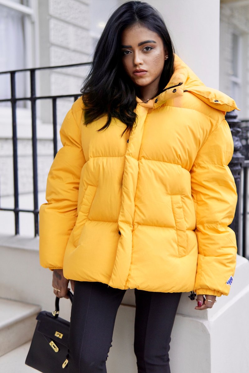 Sachini wearing a yellow Diesel puffer jacket holding a black Hermès Kelly bag