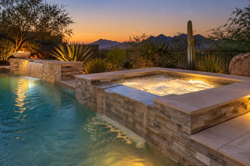 Glowing spa beside a pool at dusk with mountains in the distance