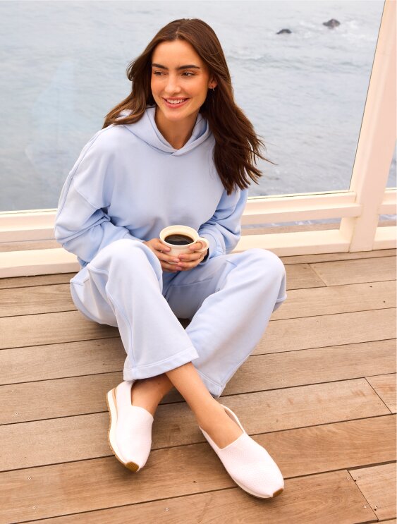 Ocean background. Model sitting, wearing Resident Plus in White Knit.
