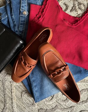 Laydown of loafers on top of knit top, jeans, and handbag.