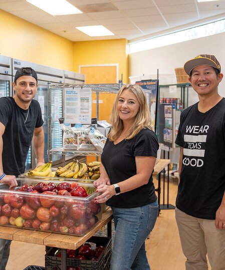 A group picture of TOMS employees in a soup kitchen shown.