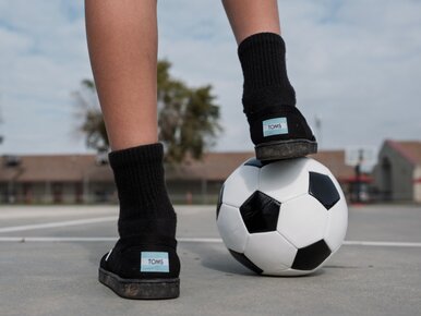 Child resting foot on soccer ball.