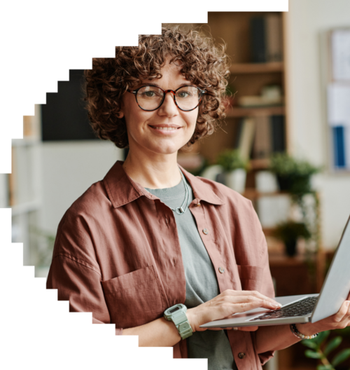 Smiling woman with curly hair and glasses, wearing a brown shirt, using a laptop in a home office setting