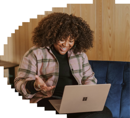 Smiling woman with curly hair on a video call, gesturing while using a Microsoft laptop on a blue couch.