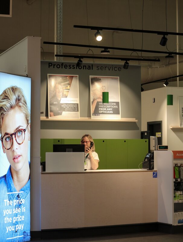 Woman at an ASDA opticians  reception desk taking a call to a patient