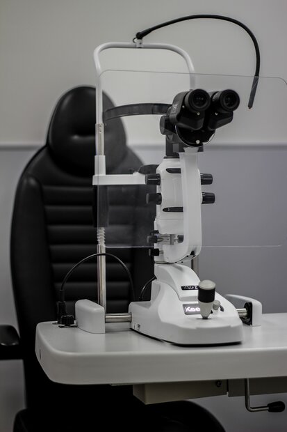 Close-up of an ophthalmic slit lamp used for eye examinations in a medical office, with a black examination chair in the background.