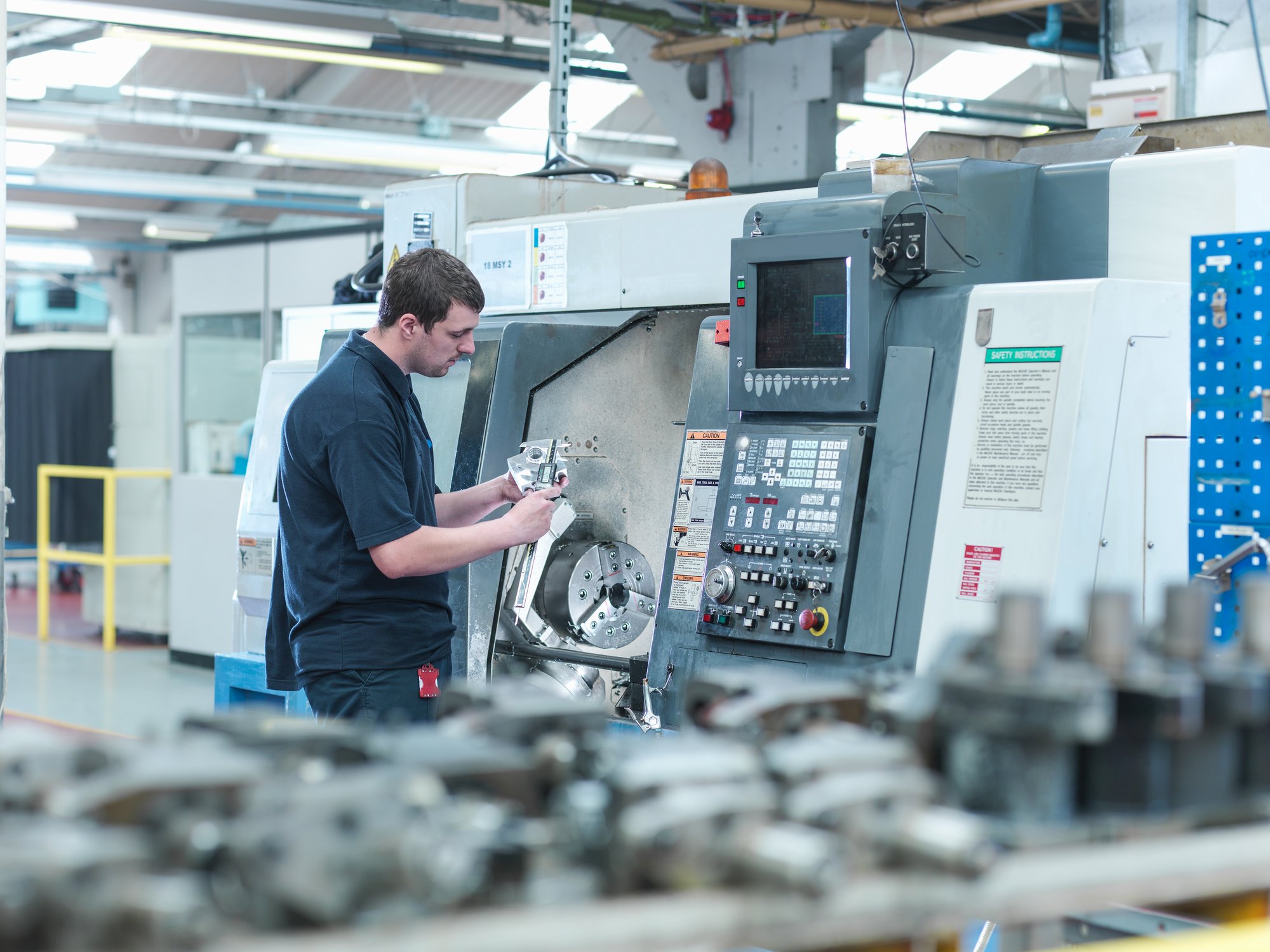 CNC machinist operator measuring a part in front of a CNC machine