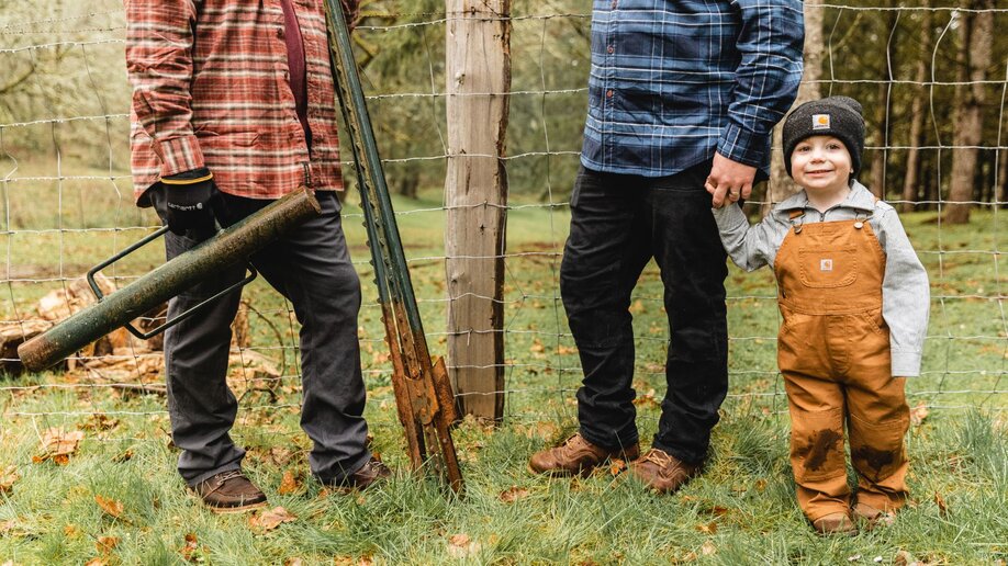 Two men and a boy standing next to a fence their yardwork clothing.