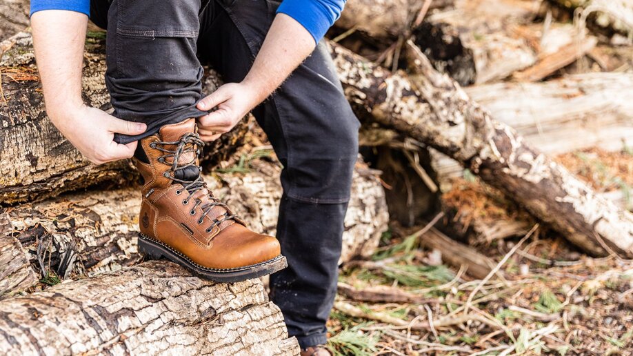 A man is tying his shoe, wearing workwear pants, for some yardwork.