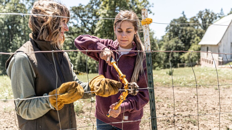 A woman and her daughter wearing gloves while repairing a fence.