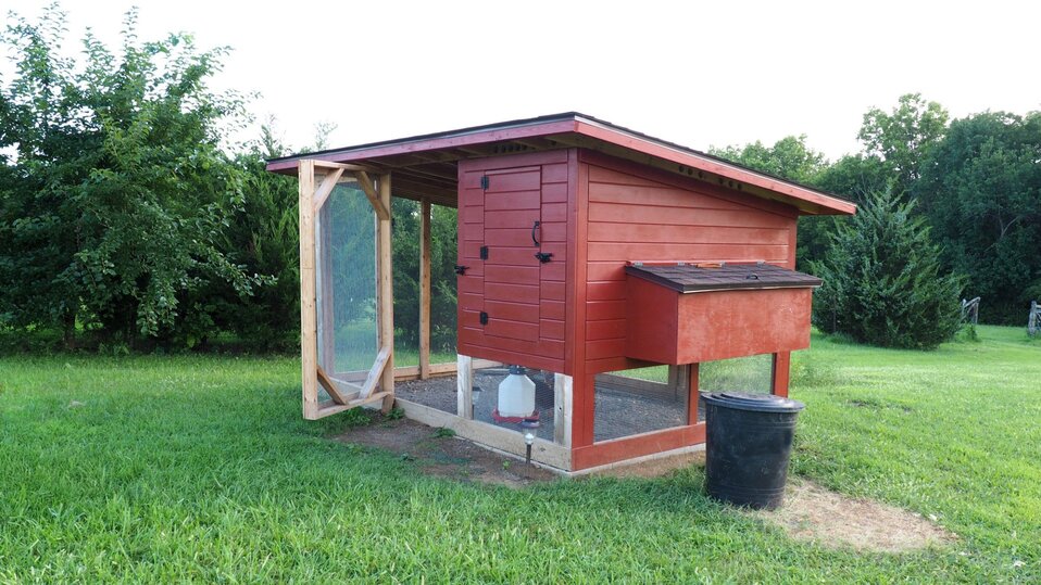 A small red chicken coop with a fenced in run area.