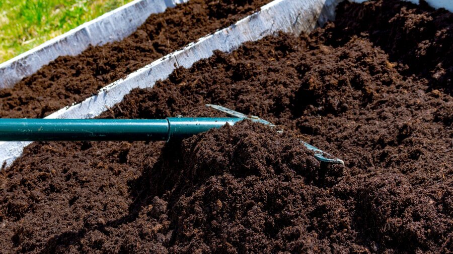 A person using a rake to mix and level their raised bed soil that's been amended with compost, nutrients, and new soil.