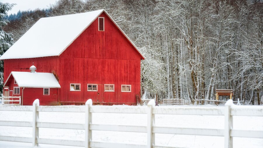 A red barn surrounded by a snowy fields and woods.