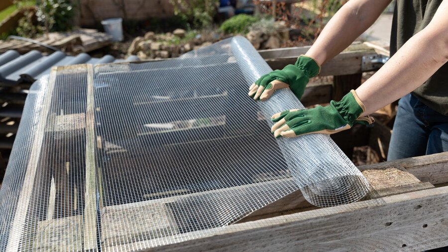 A person is covering a raised bed with netting to keep out garden pests.