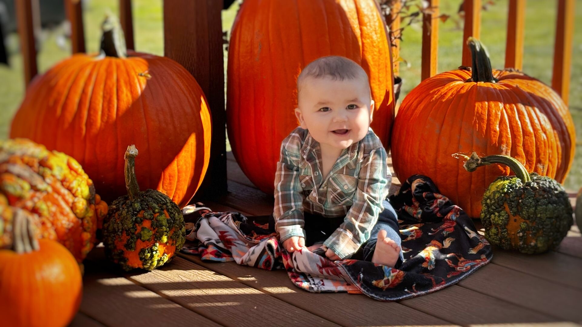 A baby sitting next to pumpkins on a porch in fall.