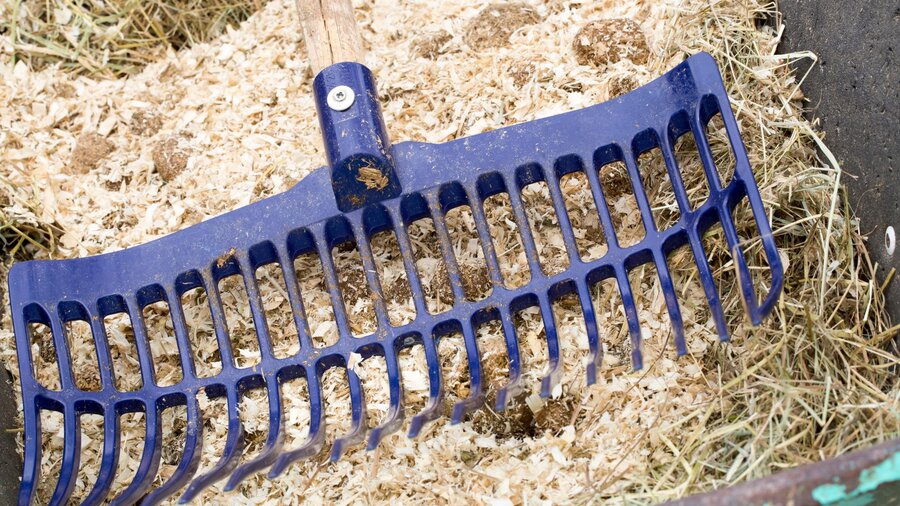 A blue rake raking up wood shavings in a horse stall.