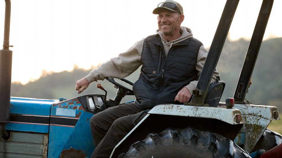A man on his tractor wearing a vest over a jacket.