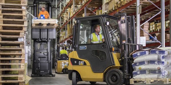 Trukki ja työntekijä logistiikkavarastossa, jossa käsitellään ja varastoidaan tuotteita turvallisesti. Kuvastaa sosiaalista vastuuta.