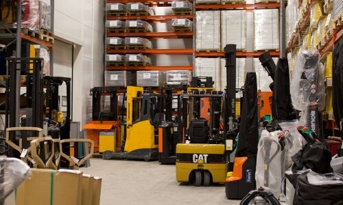 Useita trukkeja ja varastolaitteita logistiikkavarastossa, osoittaen taloudellista vastuuta