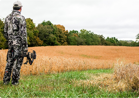 A hunter in camouflage looks over a food plot on his deer farm.