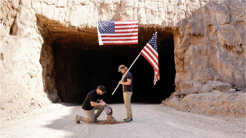 Two men in front of the Redmond Salt Mine. One holds an American flag and the other is setting up a deer mineral site.