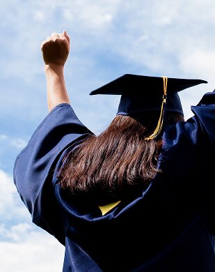 girl wearing graduation robe with hands in the air celebrating