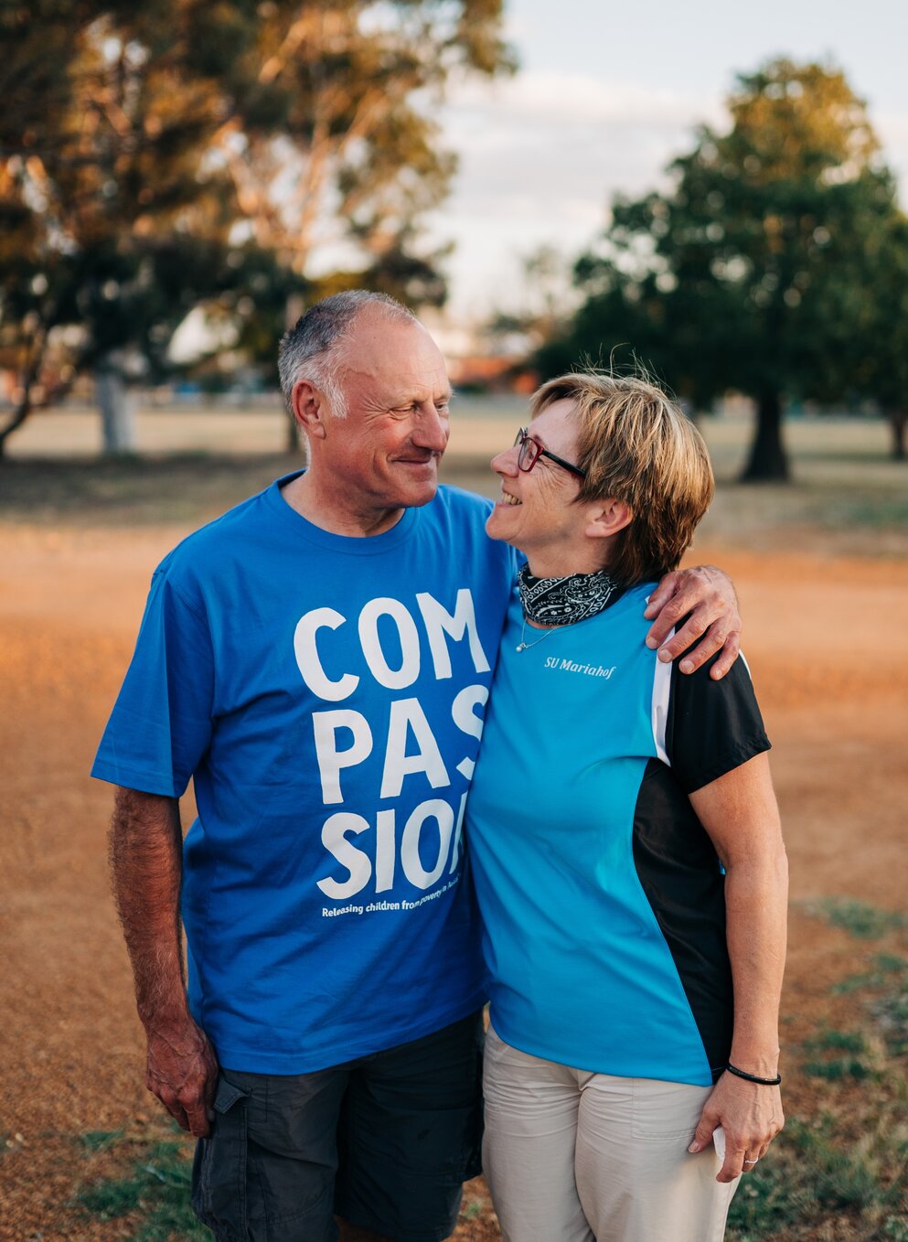 Two adults standing outdoors smiling at each other