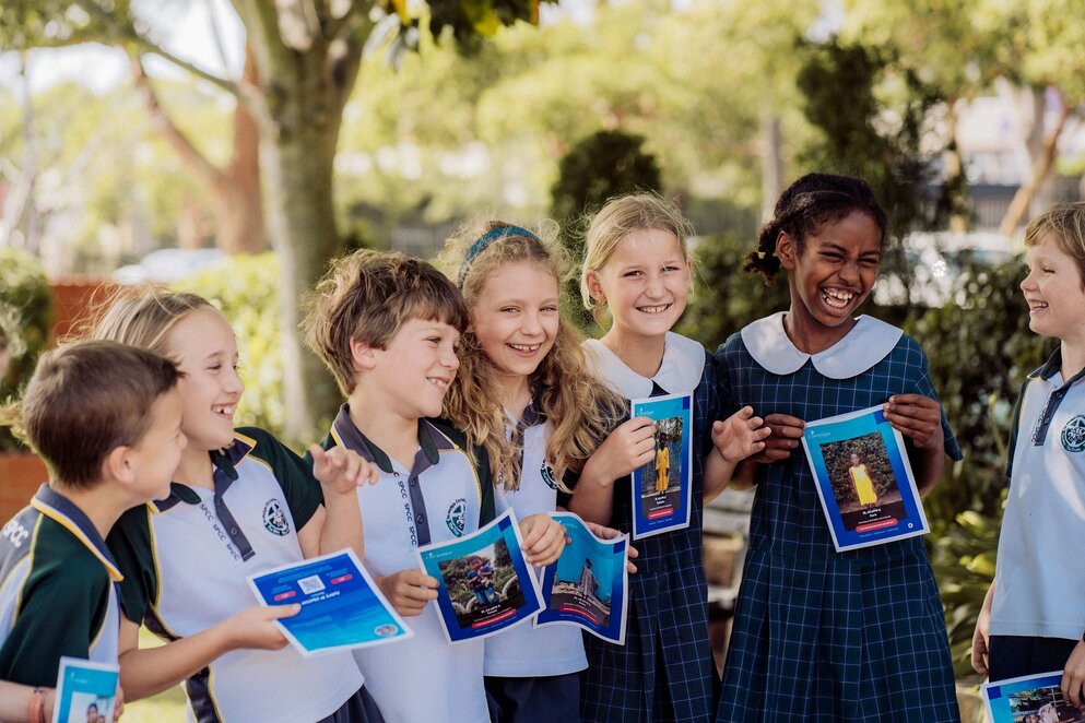 Students holding booklets and smiling outdoors
