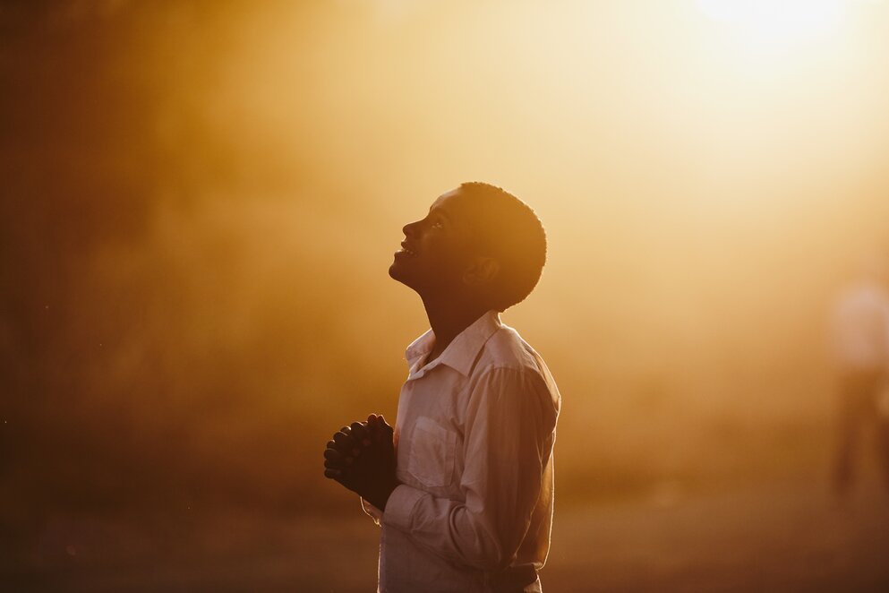 a boy looking to the sky with his hands clasped
