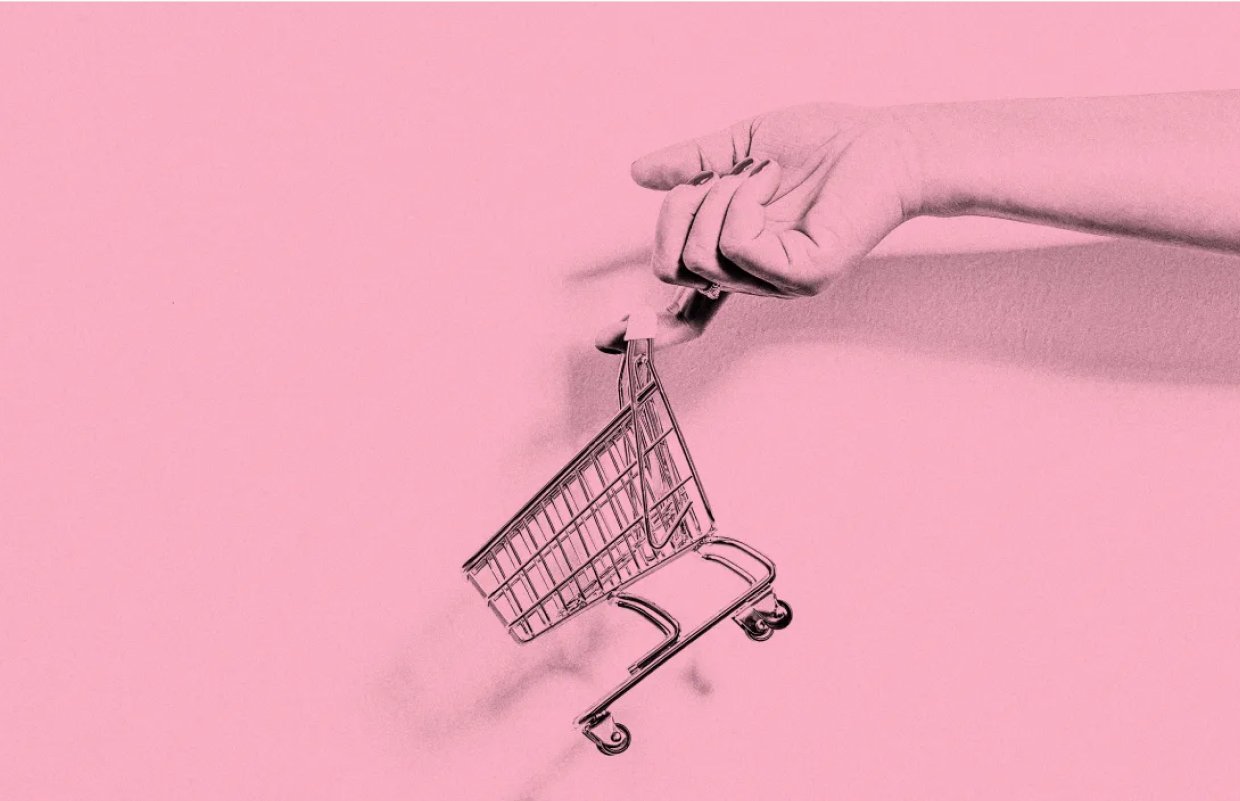 Black and white photo of a finger with a shopping cart dangling off of it on a pink background.