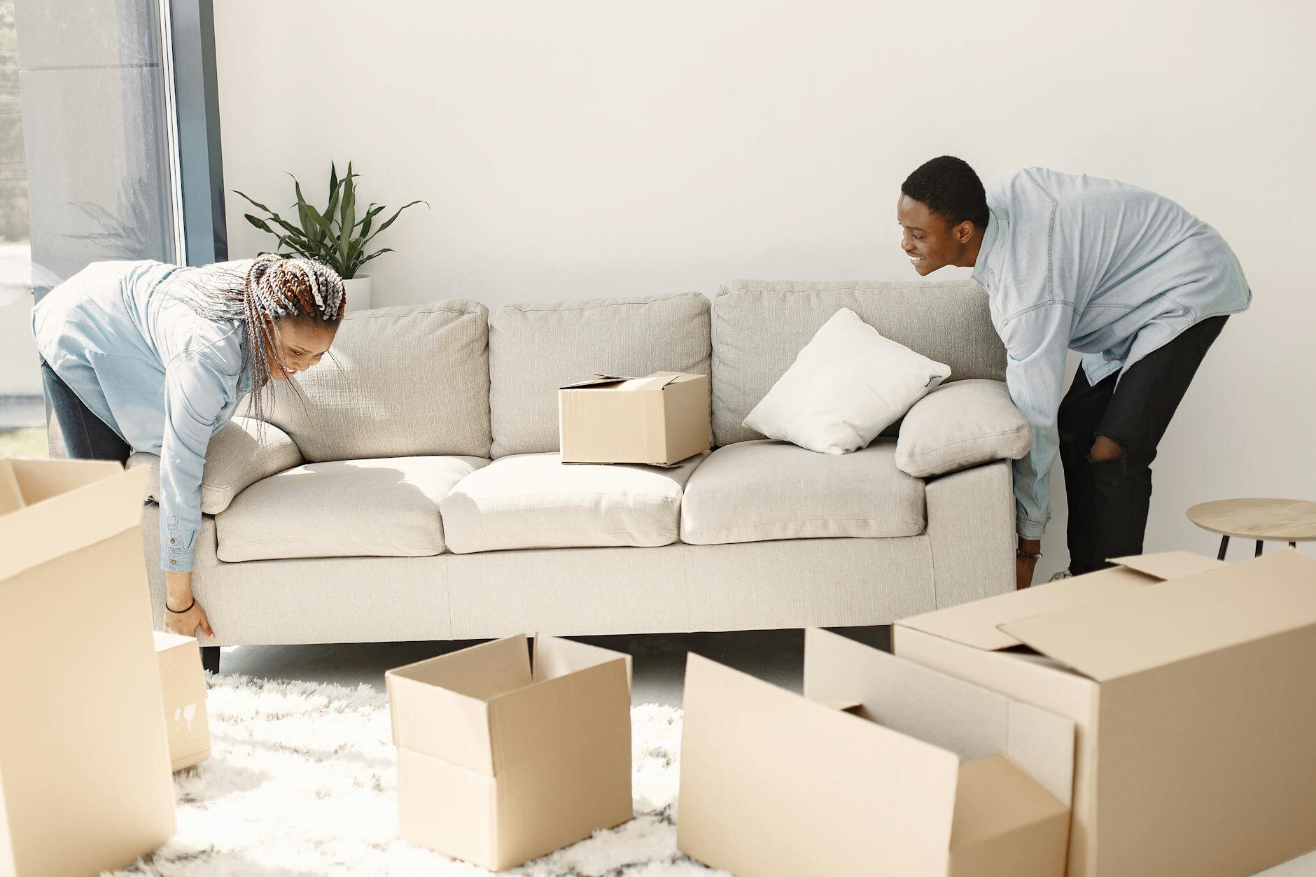 A young couple moving couch after reviewing a city map and home listings and buying in a city that is best for first-time homebuyers