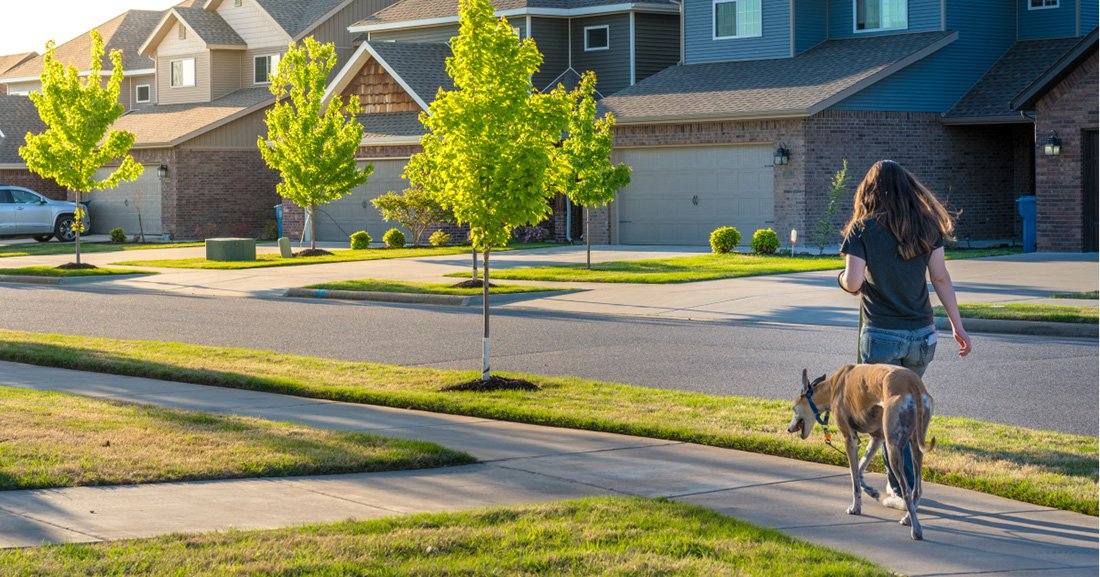 Woman walks dog through neighborhood on nice day