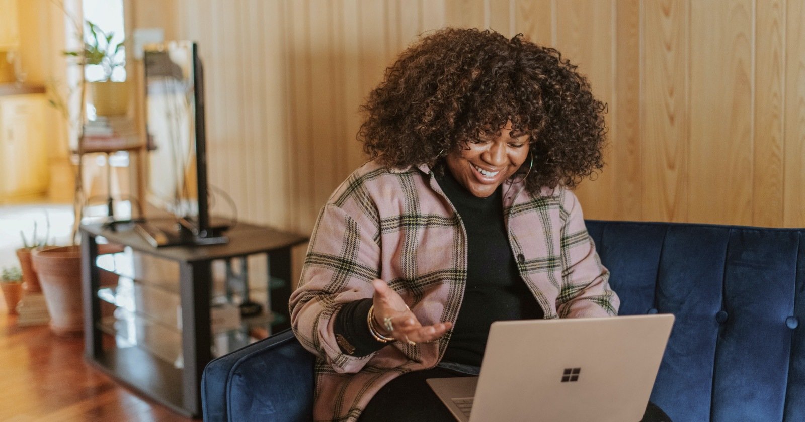 Person Sitting on Blue Couch Reacting Positively to Something on Laptop