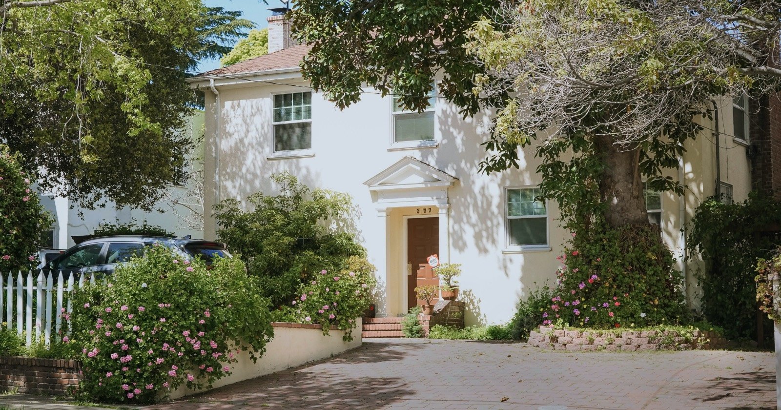 White Home with Surrounded by Flower Bushes and Trees on a Sunny Day