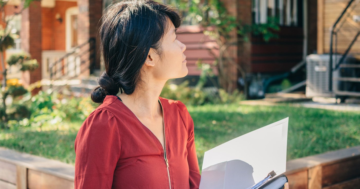 Woman in a Red Top with Open Notebook in Hand Looking at Brick Homes