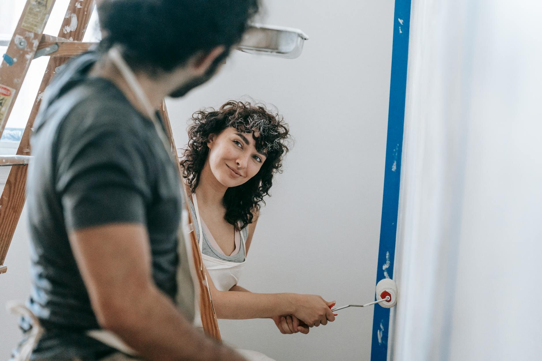 Woman painting a wall at home, smiling and looking at her husband, illustrating a home improvement project funded by a HELOC.